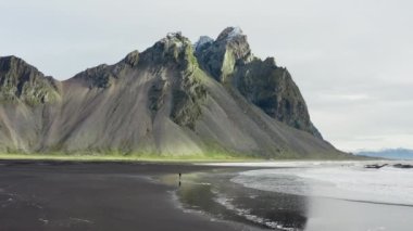 Vestrahorn Dağı, İzlanda 'ya doğru koşan adamın kara kumsaldaki insansız hava aracı çekimi.