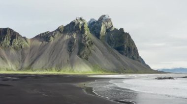 Vestrahorn Dağı, İzlanda 'yı görmek için kollarını kaldıran adamın kara kumsalda çekilmiş fotoğrafı.
