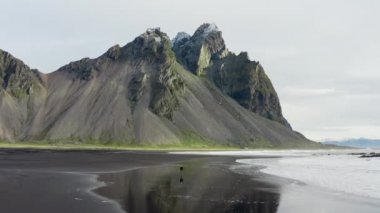 Vestrahorn Dağı, İzlanda 'dan gelen kara kumsaldaki adamın insansız hava aracı görüntüsü.