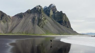 Vestrahorn Dağı, İzlanda 'dan gelen, kara kumsalda çömelmiş ve gelgitten kaçan bir adamın robot resmi.