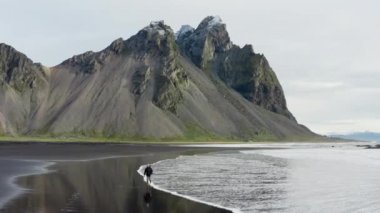 Vestrahorn Dağı, İzlanda 'dan gelen kara kumsalda yürüyen bir adamın robot resmi.