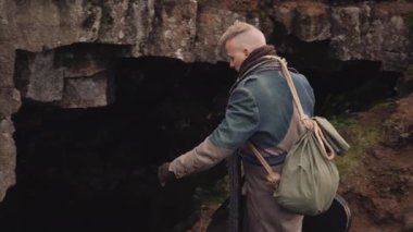 Gitar çantalı uzun paltolu adam mağaraya giriyor.