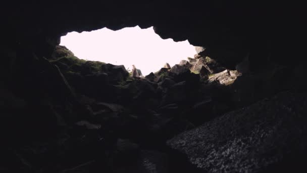 Человек в длинном пальто с футляром для гитары идет в пещеру — стоковое видео