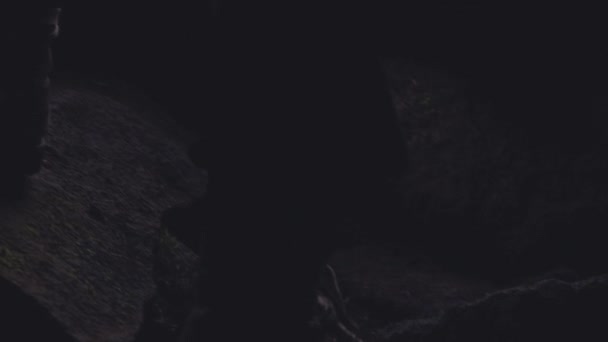 Medium Tracking Lenta Moción de disparo de hombre en botas caminando sobre rocas para salir de la cueva oscura, Islandia — Vídeos de Stock