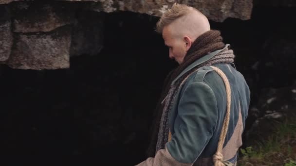 Человек в длинном пальто с футляром для гитары идет в пещеру — стоковое видео