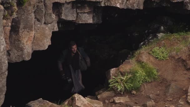 Человек в длинном пальто с футляром, покидающий пещеру — стоковое видео
