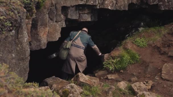 Man In Long Coat With Guitar Case Walking Into Cave — Stock Video