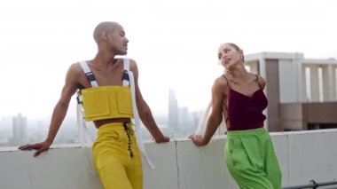 Moda kıyafetli dansçılar çatıda poz verip gülümsüyor.