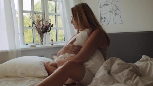 Kobieta siedzi na łóżku i przytula poduszkę rano — Wideo stockowe