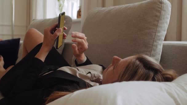 西装革履的女商人躺在沙发上打电话给智能手机 — 图库视频影像