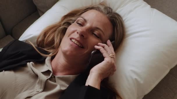 Bizneswoman leży na poduszce na kanapie i mówi na smartfonie — Wideo stockowe