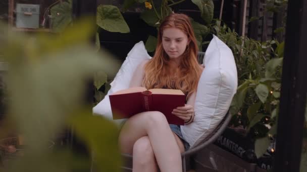 Adolescente assise sur une chaise de jardin avec oreillers et lecture — Video