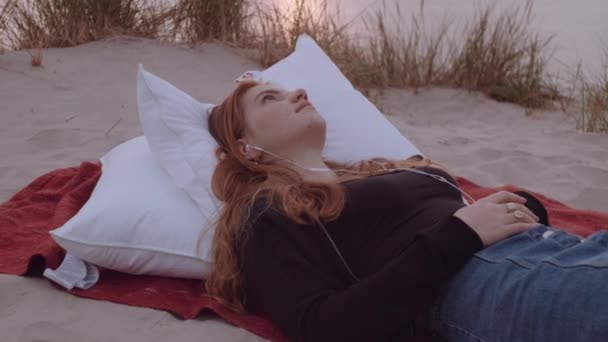 Yastıklarda yatan genç kız ve kumsalda battaniye — Stok video