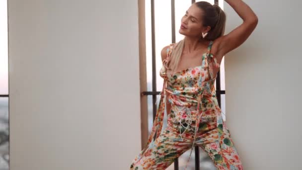 Junge Frau in floraler Latzhose tanzt an vergitterten Fenstern — Stockvideo