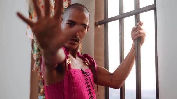 Männliche Tänzerin in rosa Mieder durch vergittertes Fenster, das in die Kamera schaut — Stockvideo