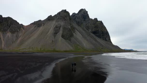 Mensen wandelen langs zwart zandstrand bij laag tij richting Estrahorn — Stockvideo