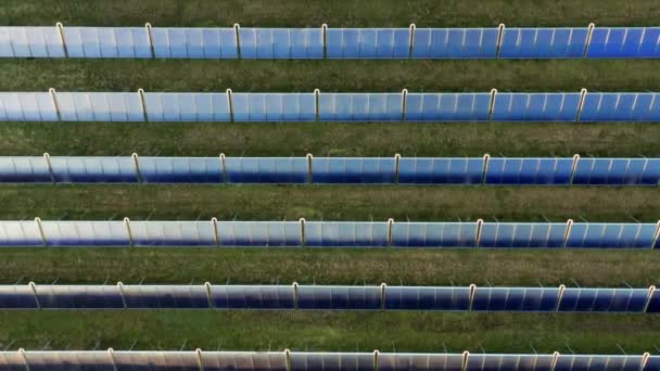 Drohne über Reihen blauer Sonnenkollektoren im Grasfeld — Stockvideo