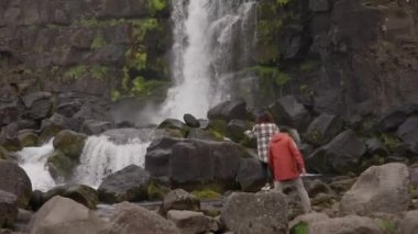 Kayaların üzerinden Oxarfoss 'a doğru adım atan çift.