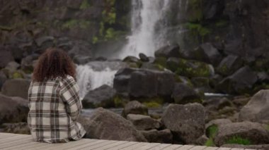Sahil yolunda bir kadın Oxarfoss Şelalesi 'ni izliyor.