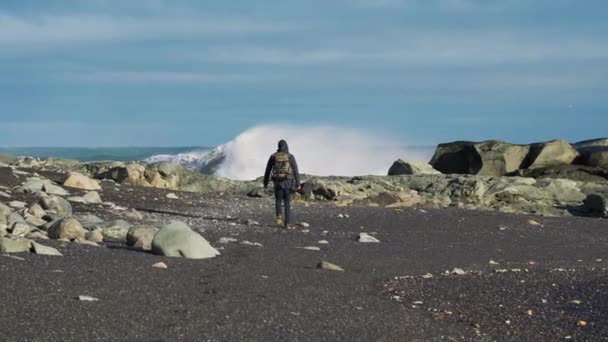 Man med ryggsäck på svart sand strand med vågor kraschar — Stockvideo