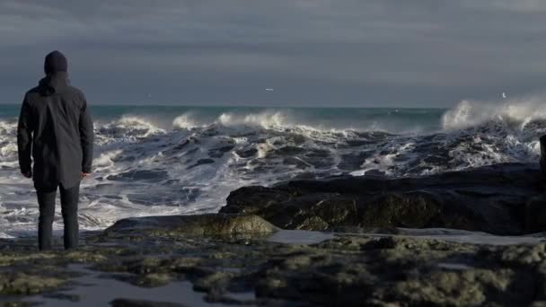 Człowiek stojący na skalistym brzegu i przenoszący się do Dodge Crashing Waves — Wideo stockowe