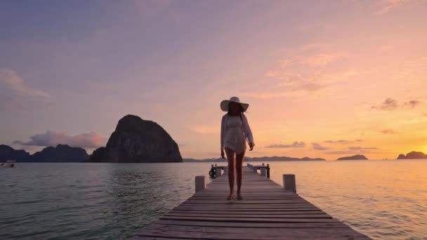 Žena kráčející po dřevěném molu jako slunce zapadá nad oceánem — Stock video