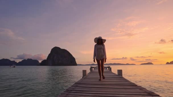 Žena kráčející po dřevěném molu jako slunce zapadá nad oceánem — Stock video
