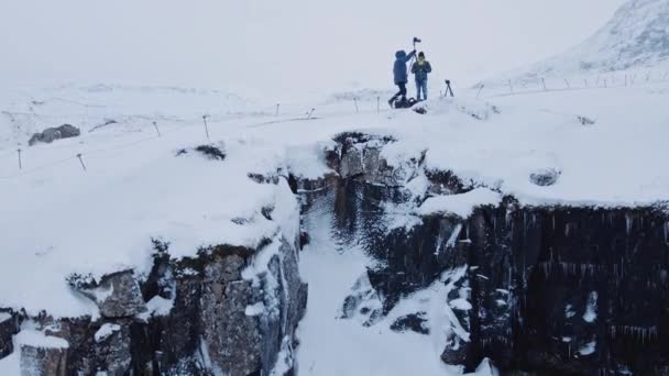 Drone che sale sulle rocce con fotografi con treppiedi nella neve — Video Stock