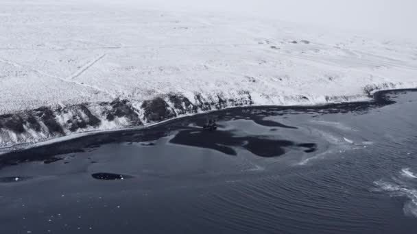 Drone à marée basse sur la plage de sable noir vers un paysage enneigé — Video