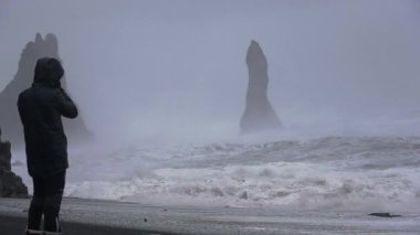 Sahilde kar fırtınasında durup dalgaları izleyen fotoğrafçı.