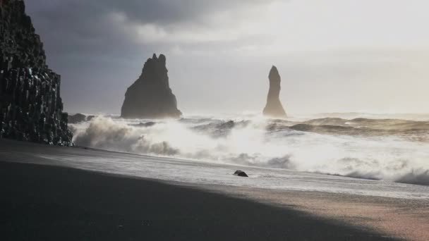 La luz del sol en la marea tormentosa que entra en la playa de arena negra y las pilas de mar — Vídeos de Stock