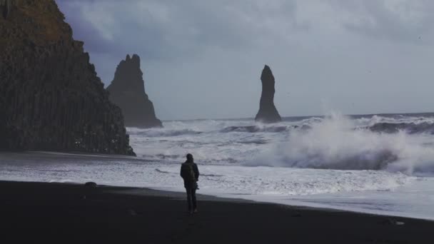 Photographer Walking On Black Sand Beach Towards White Surf — ストック動画