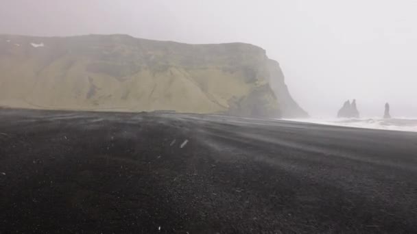 Neve caindo na praia de areia preta com pilhas de mar e montanha — Vídeo de Stock