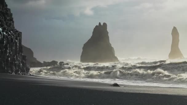 Mar tempestuoso iluminado do sol que bate em rochas e na praia preta da areia — Vídeo de Stock