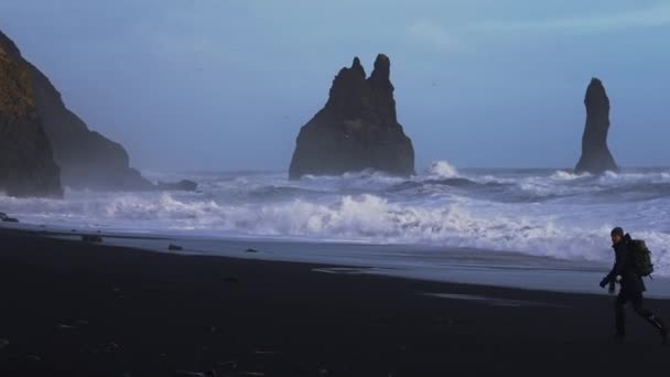 Fotograaf rent langs zwart zandstrand naar ruwe zee — Stockvideo