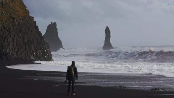 Fotógrafo en la playa de arena negra viendo mar áspero — Vídeos de Stock