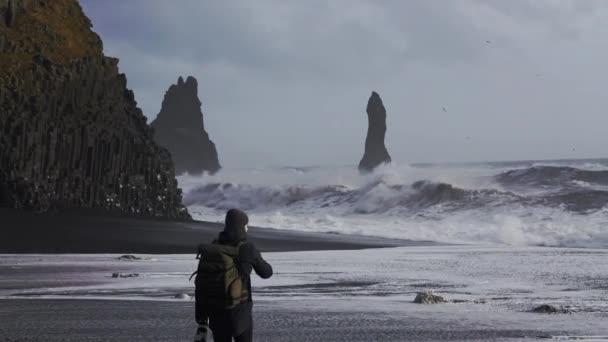 Fotograaf wandelen langs zwart zand strand naar ruwe zee fotograferen — Stockvideo