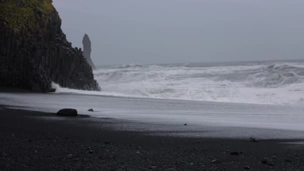 Olas que se estrellan contra rocas en la playa de arena negra — Vídeo de stock