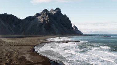 Drone, Vestrahorn manzaralı, dalgaların üstünde ve sahilde yükseliyor.