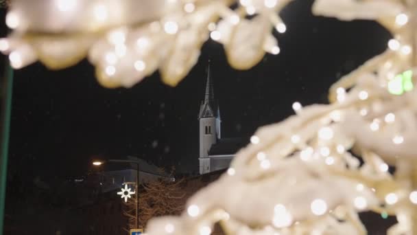 Luces de hadas iluminadas en árbol de Navidad y campanario de la iglesia — Vídeos de Stock