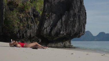 Genç bir kadın kumsalda güneşleniyor.