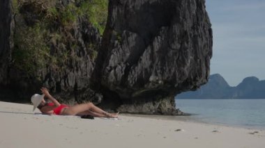 Genç kadın plajda güneşlenmek için güneşleniyor.