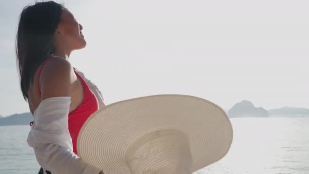 Femme mettant sur le chapeau de soleil tout en marchant dans la mer au large de la plage Entalula — Video