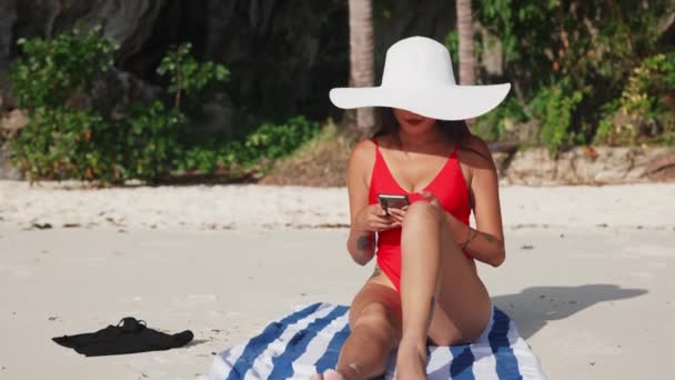 若い女性はスマートフォンでビーチに座っています — ストック動画