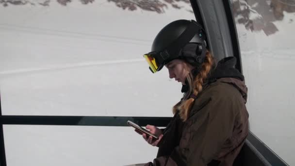 Vrouw in Skikleding die opkijkt vanaf de telefoon in de kabelbaan — Stockvideo