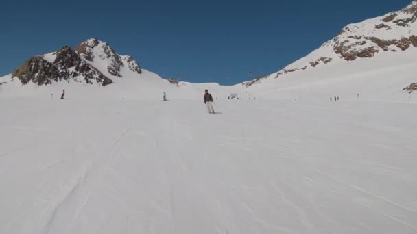 Mujer esquiando rápidamente por la pista de esquí de montaña bajo el cielo azul — Vídeo de stock