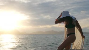 Bikini Giyen Genç Kadın ve Denizde Duran Güneş Şapkalı Kadın