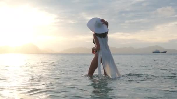 Mujer joven en bikini y sombrero de sol en el mar al atardecer — Vídeos de Stock