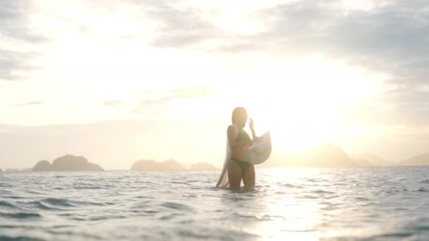 Kobieta w bikini i kapeluszu, stojąca na morzu o zachodzie słońca — Wideo stockowe