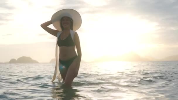 Mujer en bikini y sombrero de sol, sonriendo en el mar al atardecer — Vídeos de Stock